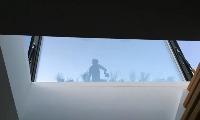 Silhouette d'une personne arrosant des plantes à travers un puit de lumière panneau sandwich.