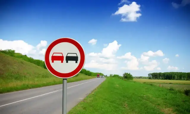 Znak zakaz wyprzedzania dla ciężarówek na tle błękitnego nieba i zielonych pól.