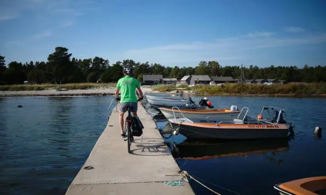 En cyklist på en brygga med båtar vid en svensk kust. Perfekt för att utforska cykelleder Sverige.