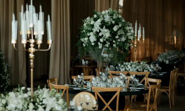 Eleganckie wesele w czarnym stylu. Stoły nakryte czarnymi obrusami, ozdobione białymi kwiatami i złotymi świecznikami.