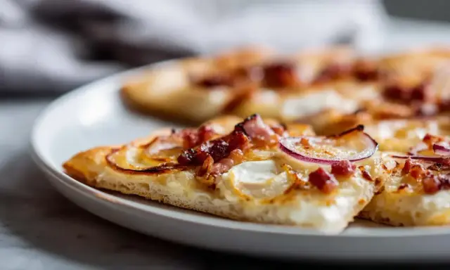 Tranches de flammekueche recette originale sur une assiette blanche, garnie de lardons, oignons rouges et fromage crémeux.