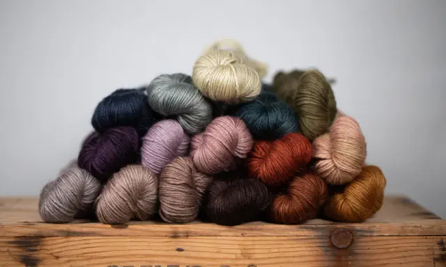 A pile of colorful yarn skeins in various earthy tones, resting on a wooden crate.