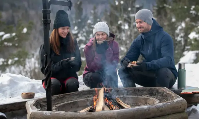 Vänner njuter av värmen från en eld och fika under härliga ute aktiviteter i snöig skogsmiljö.