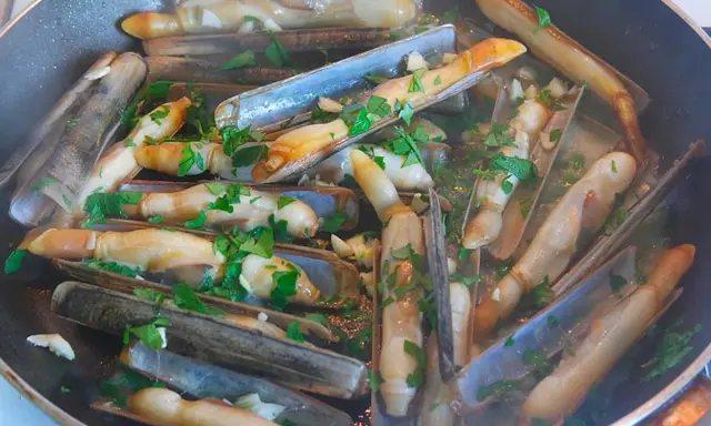 Couteaux en persillade cuits dans une poêle, parsemés de persil frais. Un plat savoureux et simple.