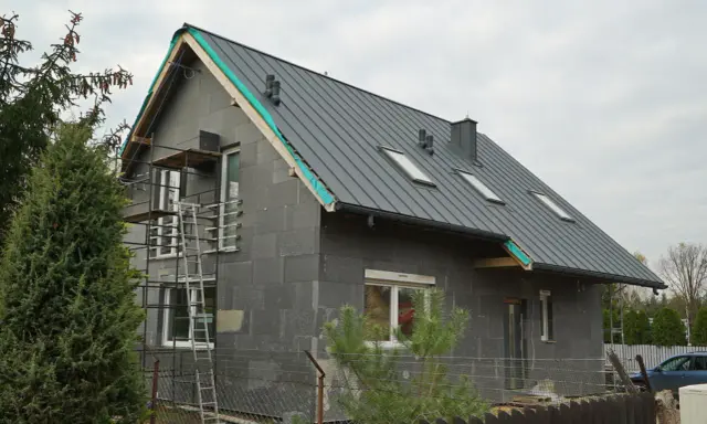 Nowy dom w budowie, z szarym dachem i oknami dachowymi. Wkrótce będzie gotowa galeria stare domy po remoncie.
