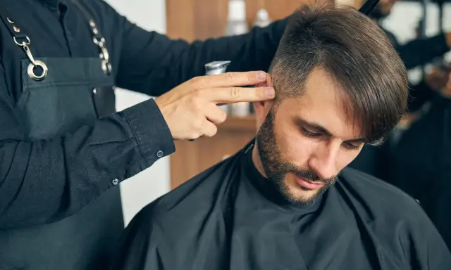 Fryzjer dopracowuje męskie fryzury z grzywką do przodu, tworząc stylowy look.