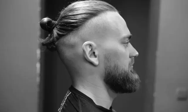 Mężczyzna z brodą i fryzurą na samuraja, z włosami upiętymi w kok na czubku głowy.