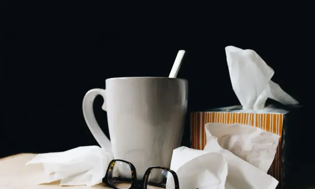 Kubek z herbatą, chusteczki i okulary. Urlop L4 nie zawsze jest wypoczynkiem.