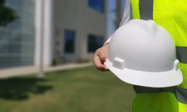 Inspektor BHP trzyma biały kask ochronny na tle budynku.