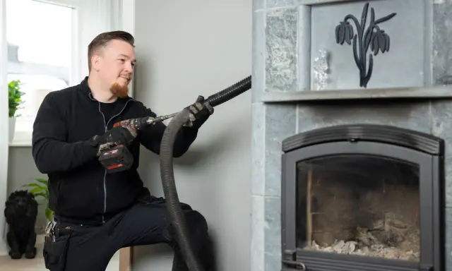 Sotare rengör en braskamin med en dammsugare. Frågar du dig "vad kostar sotning av braskamin"?