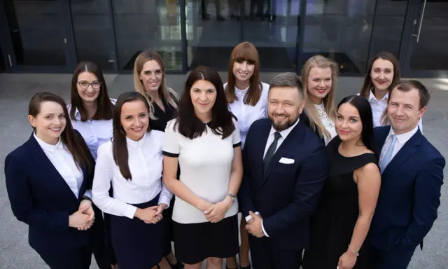 Grupa prawników w garniturach i strojach biznesowych pozuje przed budynkiem.