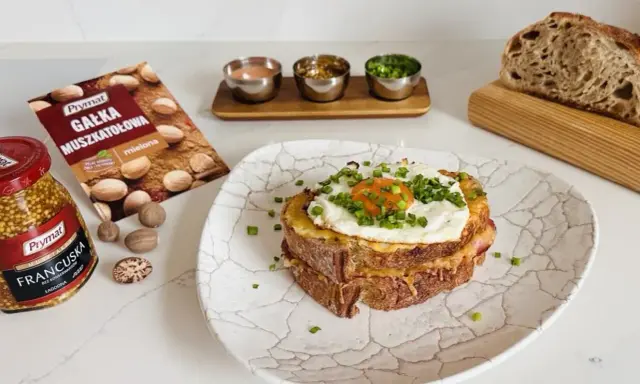 Pyszny croque madame z jajkiem sadzonym i szczypiorkiem, obok musztarda francuska i gałka muszkatołowa.