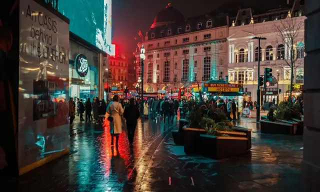 Luci al neon e riflessi sull'asfalto bagnato, la vibrante vita notturna londra pulsa tra la folla e gli edifici storici illuminati.