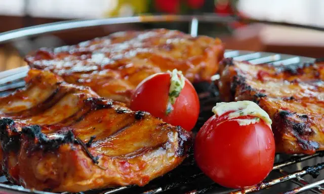 Costillas de cerdo y tomates rellenos en una parrilla. El tiempo que tarda el carbón en hacer brasa es clave para esta deliciosa cocción.