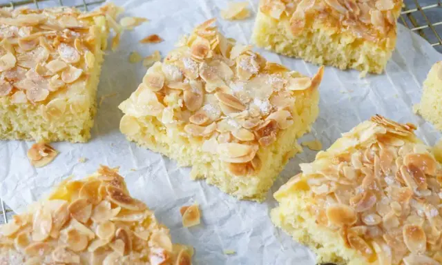 Saftiger Buttermilch Kuchen mit knusprigen Mandelblättchen und Zucker bestreut, auf Backpapier und einem Gitterrost angerichtet.