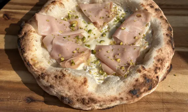 Pizzateig mit Hefe, belegt mit Mortadella und Pistazien. Der Rand ist luftig und leicht angekohlt.