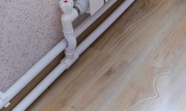 Białe rury grzewcze biegną wzdłuż ściany. Woda na podłodze sugeruje, że to dobry pomysł na zasłonięcie rur, by uniknąć takich sytuacji.