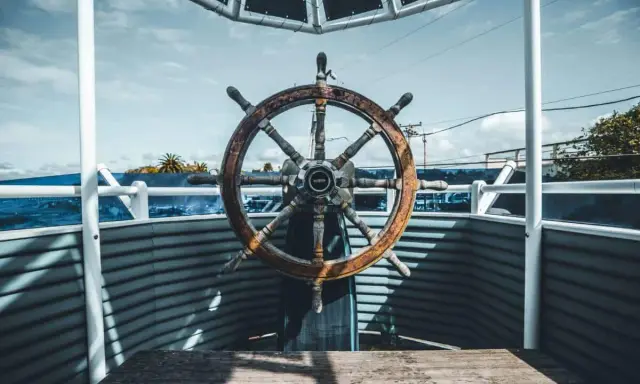 Roue de gouvernail en bois patiné, prête à barrer un bateau vers l'horizon bleu.