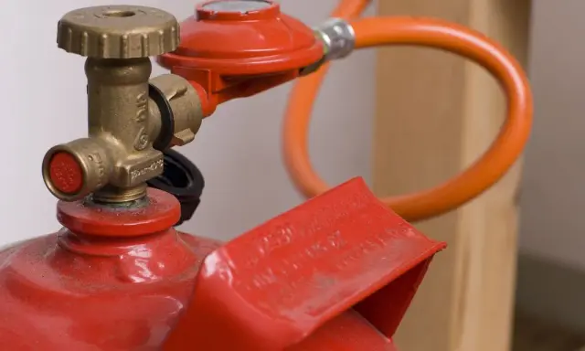 Détail d'une bouteille de propane rouge avec détendeur et tuyau orange, illustrant la norme d'installation gaz propane bouteille.