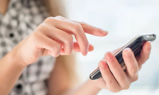 Dłoń trzymająca smartfon, palec wskazujący dotyka ekranu.
