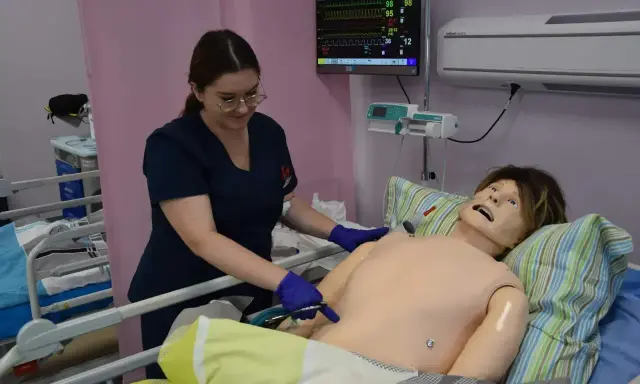 Studentka stomatologii ćwiczy procedury medyczne na fantomie. Monitor parametrów życiowych pokazuje dane.
