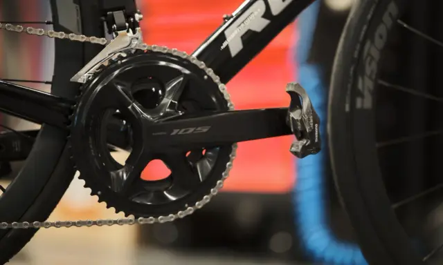 Szukasz informacji, jak dobrać korbę do roweru? Zobacz zbliżenie na czarną korbę Shimano 105 z łańcuchem i pedałem.