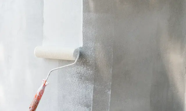 Rodillo blanco aplica pintura a pared gris. Se ve el proceso de cuantas manos de pintura se le da a una pared para un acabado perfecto.