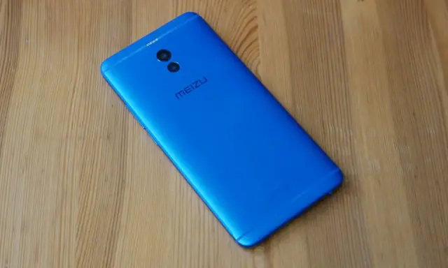 Niebieski smartfon Meizu M6 Note z podwójnym aparatem z tyłu leży na drewnianym blacie.