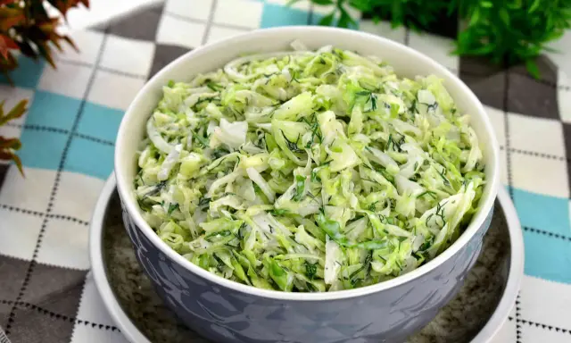 Pyszna surówka z białej kapusty z koperkiem, podana w szarej misce na wzorzystym obrusie.