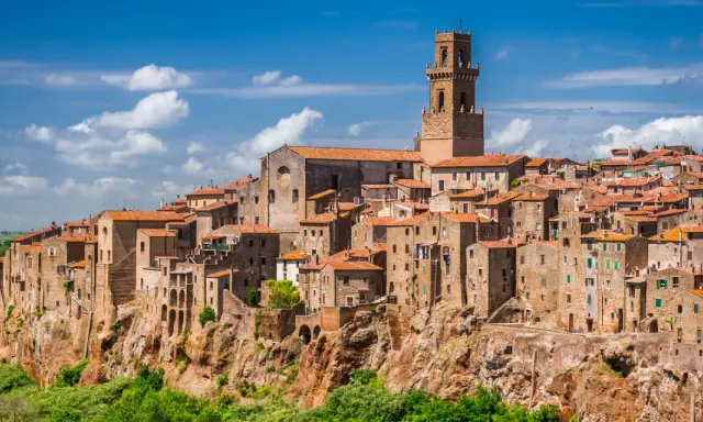 Eine malerische Stadt in der Toskana thront auf einem Felsen, umgeben von grünen Hügeln und blauem Himmel mit Wolken.
