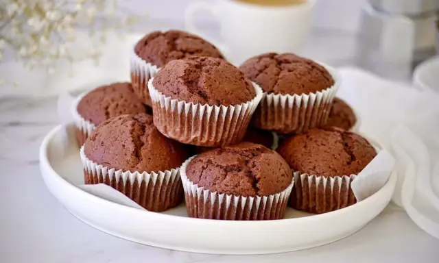 Ein Stapel saftiger Schoko-Muffins, die wie **red velvet muffins** aussehen, auf einem weißen Teller. Im Hintergrund eine Kaffeetasse.