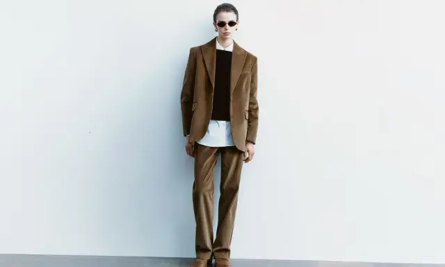 Model in a brown corduroy suit, white shirt, and black sweater, wearing sunglasses.