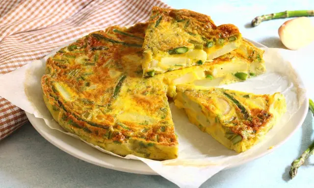 Una gustosa frittata di asparagi, con patate e uova dorate, tagliata a fette su un piatto bianco.