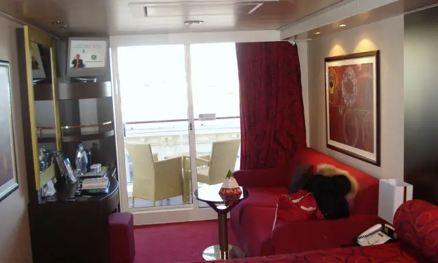 Cabina su MSC Divina, ponte 9, con balcone, divano rosso, letto e quadro astratto.