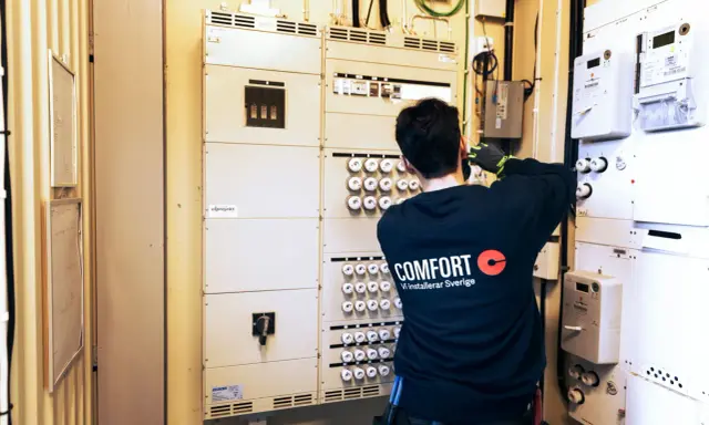 En elektriker arbetar vid en elcentral med många säkringar och mätare. För säkerheten måste man ha jordfelsbrytare.