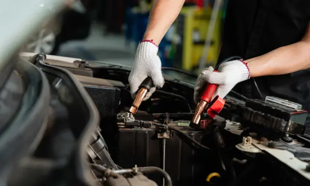 Manos enguantadas conectando cables a la batería del coche. Es hora de desconectar la batería del coche para un mantenimiento seguro.