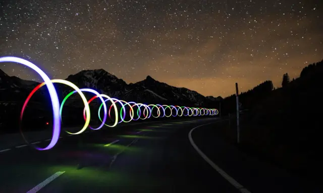 Una carretera nocturna bajo un cielo estrellado, con aros de luz de colores que parecen flotar. ¡Trucos fotos geniales!