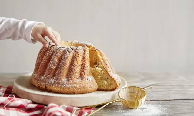 Un enfant touche un Kougelhopf, une des spécialités alsace, saupoudré de sucre glace. Une tranche est coupée, révélant des raisins secs.