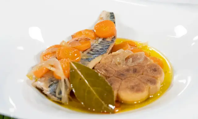 Deliciosa caballa en escabeche con zanahorias, cebolla y laurel en un plato blanco.