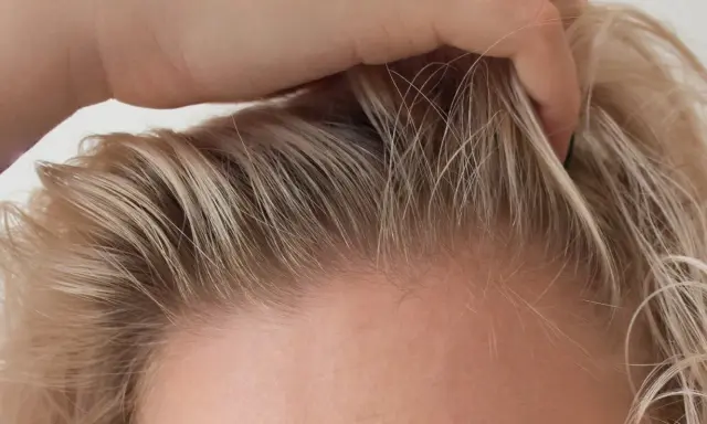Dłoń delikatnie przeczesuje jasne włosy, ukazując drobne kosmyki, które zdradzają, jak ujarzmić baby hair.