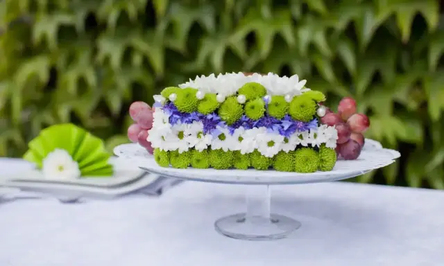Inspiracja na bukiety na stół weselny: kwiatowy tort z chryzantem, chabrów i winogron na paterze.