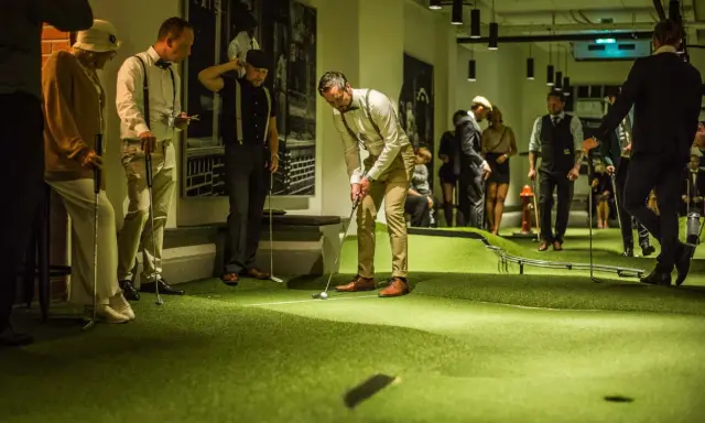 Människor i festliga kläder spelar minigolf på Golfbaren Stockholm.