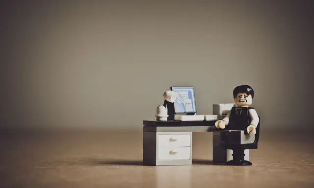 Figurka Lego przedstawiająca zestresowanego pracownika siedzącego przy biurku z komputerem.