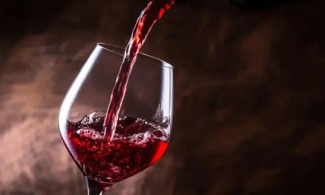 Vino tinto se vierte en una copa, creando burbujas y espuma. Un brindis por el día del vino.