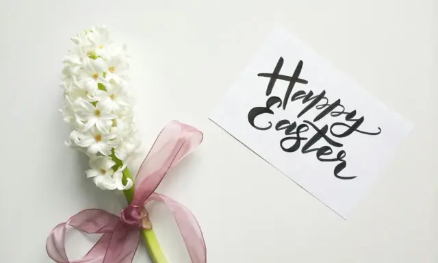 Un giacinto bianco legato con un nastro rosa, accanto a un biglietto con scritto "Happy Easter". Come una poesia campane di Pasqua di Gianni Rodari.