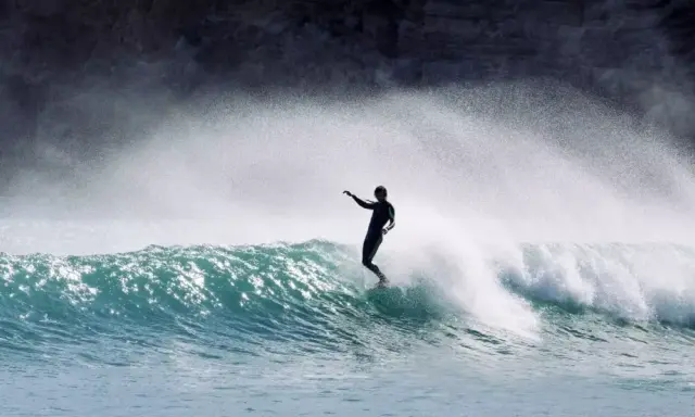 Surfer in Aktion auf einer Welle an der Algarve. Die Gischt spritzt, während er die portugiesische Küste genießt.