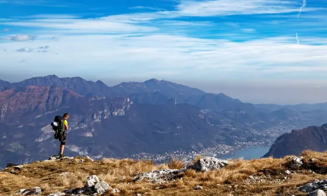 Escursionista ammira la vista panoramica di una montagna vicino Milano, con un lago e un paese in lontananza.