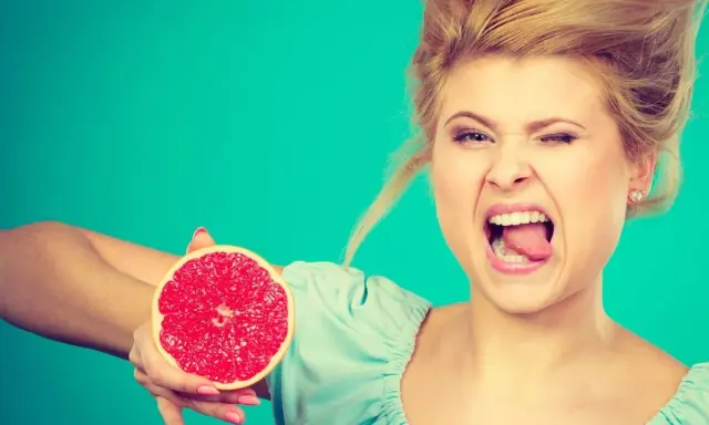 Kobieta z miną, jakby spróbowała gorzkiej spermy, trzyma połówkę grejpfruta.