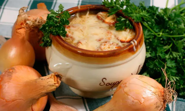 Un bol de soupe à l'oignon gratinée, un plat parisien réconfortant, entouré d'oignons frais et de persil.