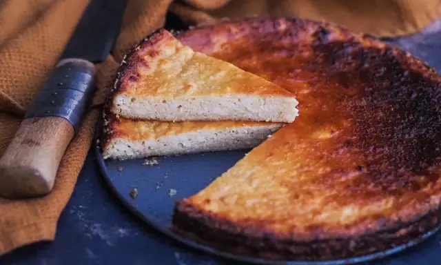 Un fiadone corse, un gâteau au fromage et au citron, est servi avec une tranche coupée, à côté d'un couteau sur un tissu ocre.